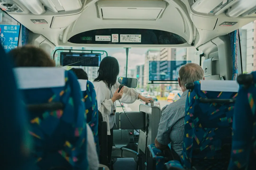 Reiseleiterin mit Mikrofon vorne in einem modernen Reisebus während der Fahrt durch eine Stadt mit Fahrgästen