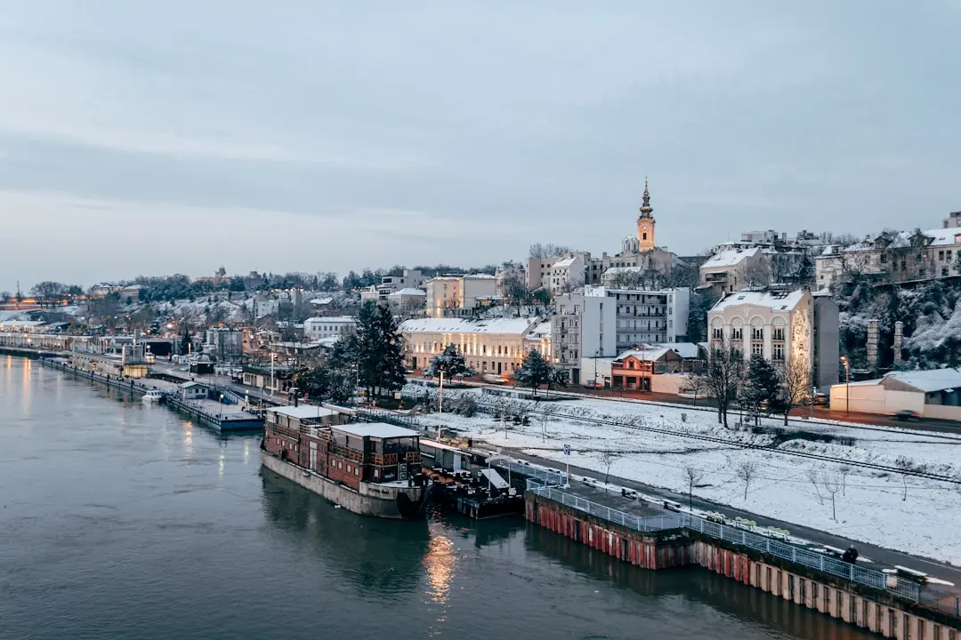 Verschneite Uferpromenade in Belgrad zur blauen Stunde mit beleuchteten Gebäuden und Schiffen an der Save