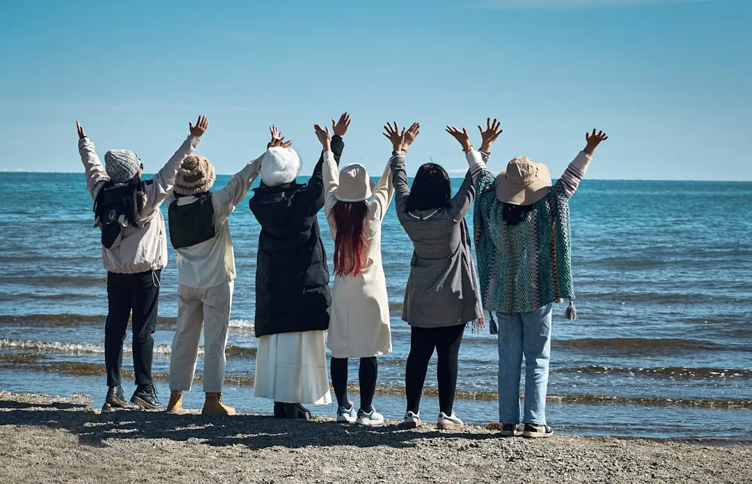 Eine Reisegruppe steht mit jubelnd erhobenen Armen am Strand vor dem blauen Meer und genießt die Gemeinschaft