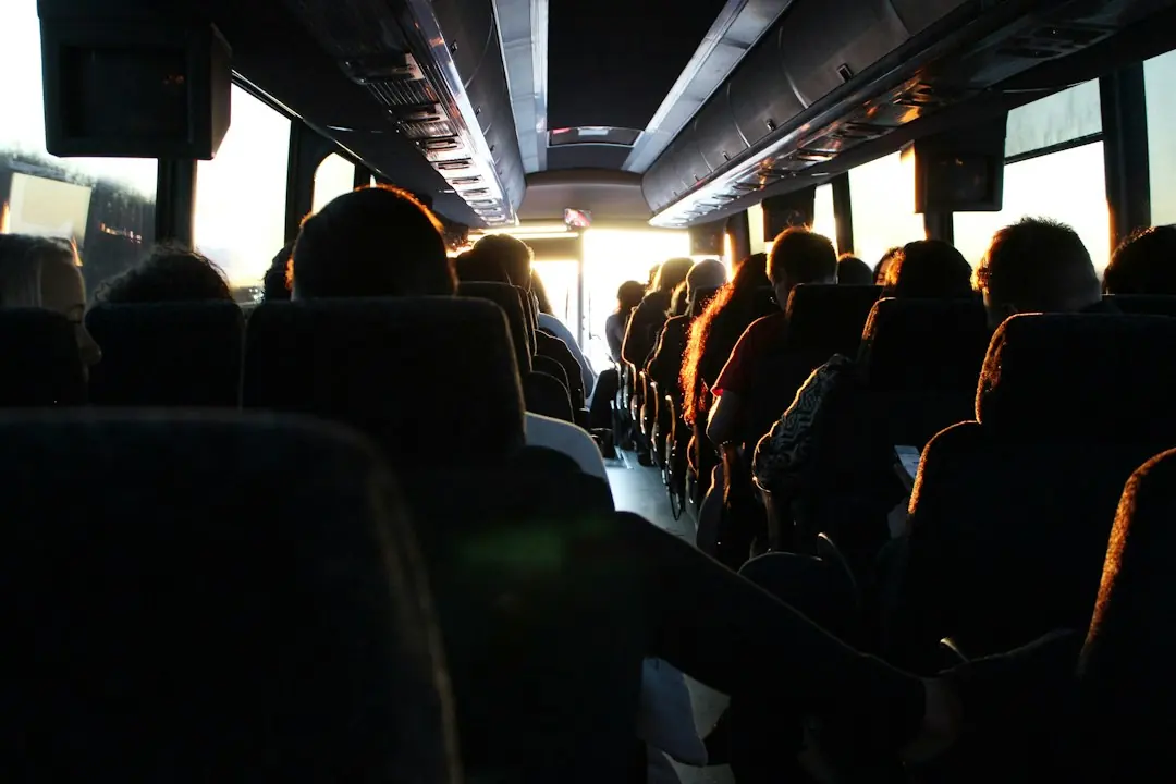 Blick von hinten durch einen vollbesetzten Reisebus, während die tiefstehende Sonne durch die Frontscheibe leuchtet