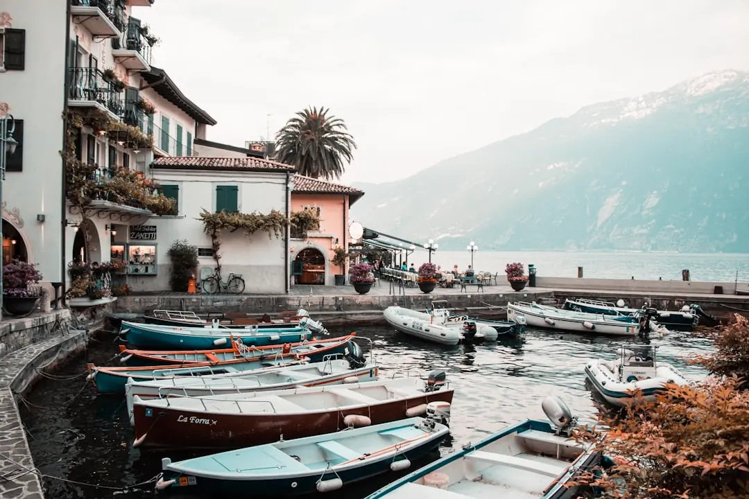 Kleine Boote im Hafenbecken von Limone sul Garda vor pastellfarbenen Häusern und steilen Bergflanken am Gardasee