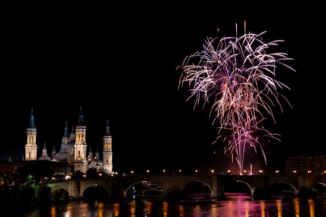 Buntes Silvesterfeuerwerk über einer beleuchteten Kathedrale und einer Bogenbrücke an einem Fluss bei Nacht