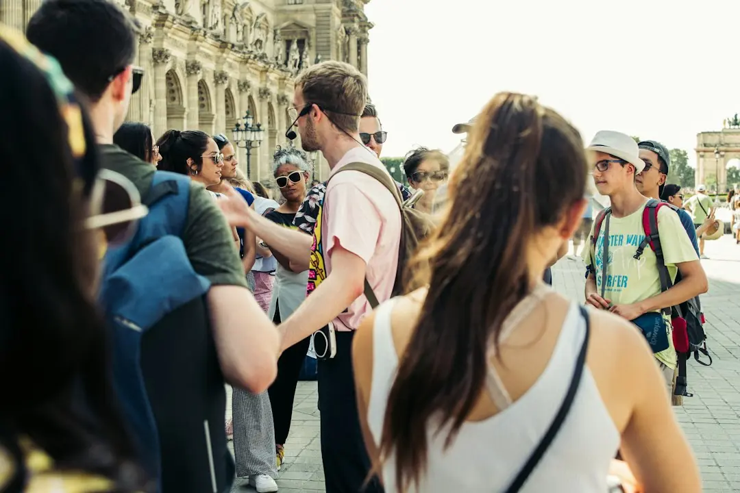 Eine Reisegruppe hört bei Sonnenschein aufmerksam einem Guide vor historischen Gebäuden in Paris zu
