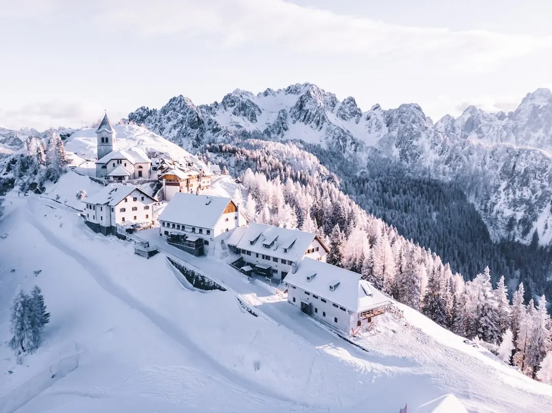 Verschneites Bergdorf auf einem Grat vor imposanter Alpenkulisse im sanften Winterlicht