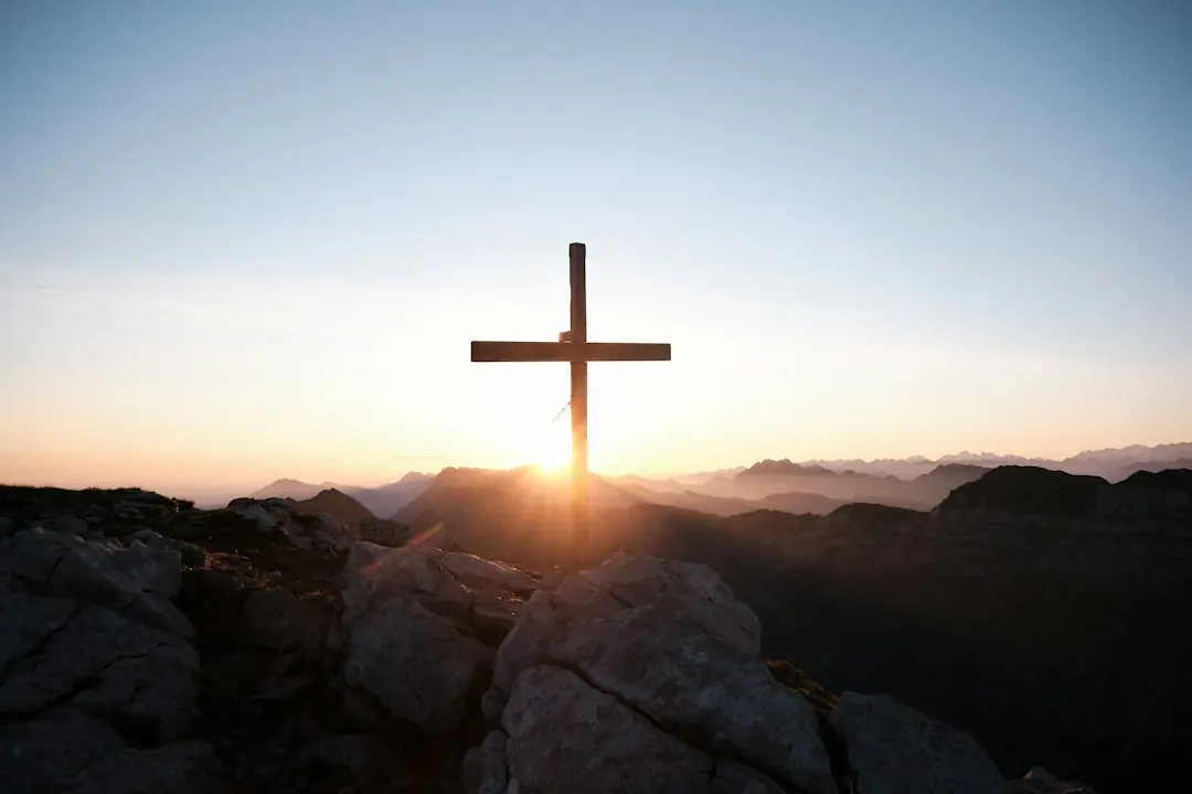 Ein hölzernes Gipfelkreuz auf felsigem Gebirge vor einem stimmungsvollen Sonnenuntergang in den Alpen